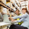 Warehouse worker and manager looking at laptop in a large warehouse